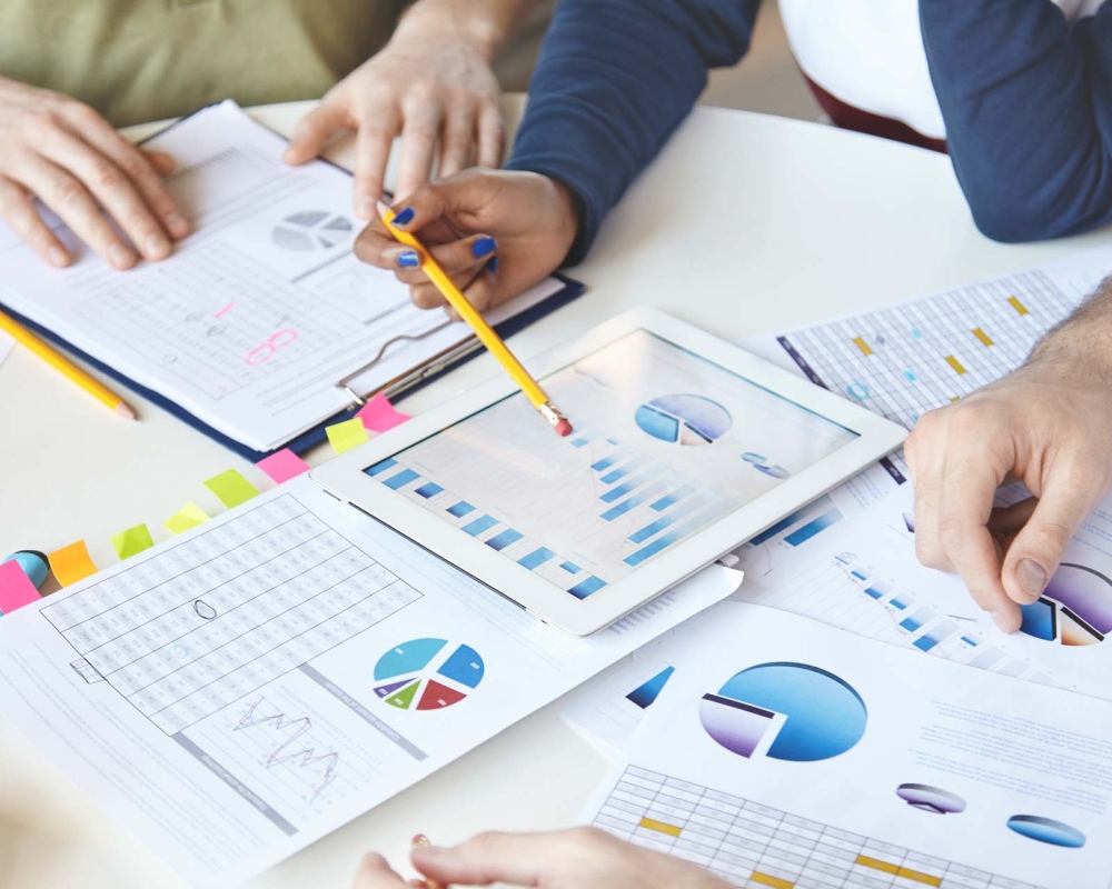 Cropped shot of people of diverse races working on business plan, analyzing value of goods, services, growth rate, making review of market situation, counting loss, using modern devices and touch pad